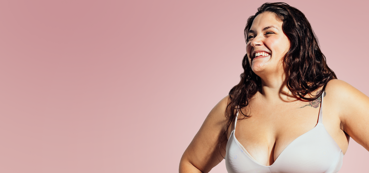 Woman wearing a white bralette against a pink background
