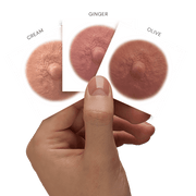 Three nipple tattoos  labeled 'Cream', 'Ginger', and 'Olive' held by a hand against a black background.