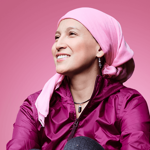 Woman wearing a pink headscarf and purple jacket against a pink background
